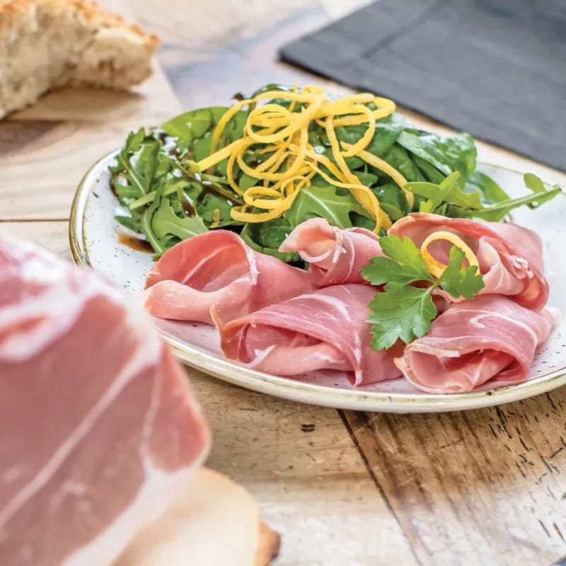 Dünne Schinkenscheiben mit Blattsalat auf einem Teller, daneben Brot