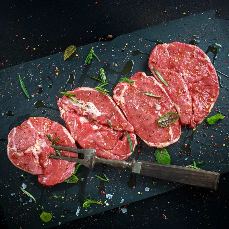 Rohe Steaks mit Kräutern und Gewürzen auf dunkler Schieferplatte